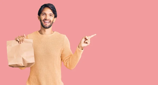 Bonito Hispânico Homem Segurando Tirar Saco Papel Sorrindo Feliz Apontando — Fotografia de Stock