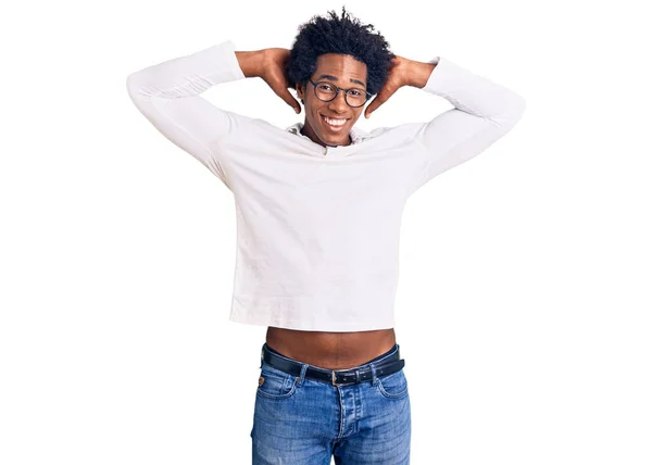 アフロの髪をしたハンサムなアフリカ系アメリカ人男性は カジュアルな服と眼鏡を身に着けてリラックスしてストレッチ 腕と手頭と首の後ろに笑顔幸せ — ストック写真