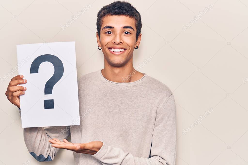 Young african amercian man holding question mark looking positive and happy standing and smiling with a confident smile showing teeth 