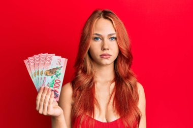 Genç kızıl saçlı kadın elinde 100 yeni Zelanda Doları banknot düşünce tarzı ve ayık yüz ifadesi kendine güvenen. 