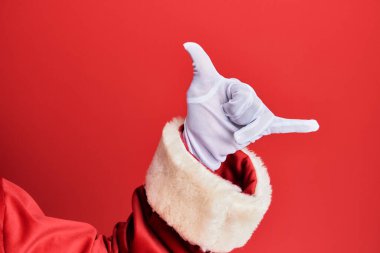 Noel Baba kostümü ve kırmızı arka planda eldivenler giyen bir adamın eli Hawaii Shaka selamlama jesti, telefon ve iletişim sembolü. 