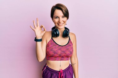 Kısa saçlı, spor giyimli, kulaklık takan, gülümseyen ve el ve parmaklarıyla 