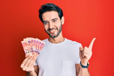 Güney Afrika Rand banknotlarını elinde tutan genç İspanyol adam gülümsüyor. 