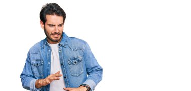 Gündelik kıyafetler giyen genç İspanyol adam tiksindirici bir ifade takınıyor ve tiksindirici bir yüz ifadesi takınıyor.. 