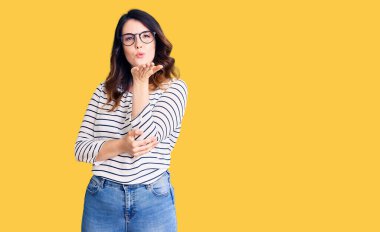 Güzel, genç, esmer, gündelik kıyafetler ve gözlük takan bir kadın kameraya bakıp havada öpücükler savuruyor. Güzel ve seksi. aşk ifadesi. 