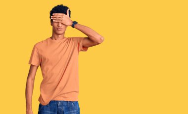 Genç, Afro-Amerikan bir adam, günlük kıyafetler giyip, elleriyle gözlerini kapatıyor, ciddi ve üzgün görünüyor. Görme, saklama ve reddetme konsepti 