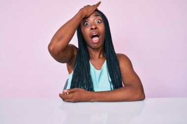 Saçları örgülü Afro-Amerikalı bir kadın masanın üzerinde oturuyor ve hata sonucu elleri üzerinde şaşırmış bir şekilde oturuyor. Hatayı unutmayın. Unuttum, kötü hafıza kavramı. 