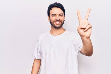 Gündelik kıyafetler giyen genç İspanyol adam iki numarayı gösterip işaret ederken kendinden emin ve mutlu bir şekilde gülümsüyor.. 