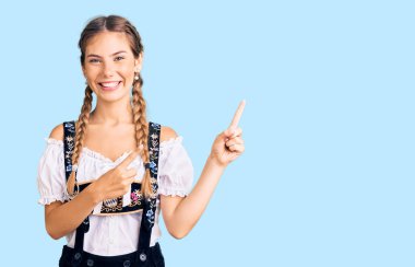 Sarışın, beyaz bir kadın. Geleneksel kıyafetler giyiyor. Gülümsüyor ve kameraya bakıyor.. 