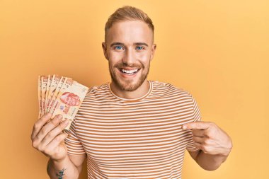 Meksika pezosu tutan genç beyaz adam mutlu bir şekilde elini ve parmağını gösterdi. 