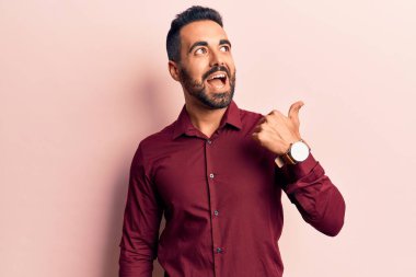 Gündelik giysiler giymiş genç İspanyol bir adam baş parmağını yana kaldırıyor ve ağzı açık gülümsüyor. 