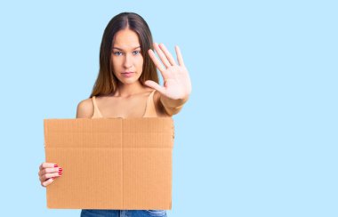 Güzel esmer, genç bir kadın elinde boş bir pankartla elinde dur işareti ile ciddi ve kendinden emin bir ifadeyle savunma jesti yapıyor. 