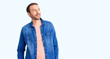 Gündelik giysiler giymiş genç yakışıklı bir adam yüzünde gülümsemeyle yan yana bakıyor, doğal bir ifade. Kendinden emin gülen. 