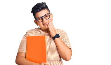 Küçük çocuk, diş ağrısı ya da diş hastalığından dolayı elinde gözlük, ağzında acı dolu bir ifade olan ağıza dokunuyor. dişçi kavramı. 