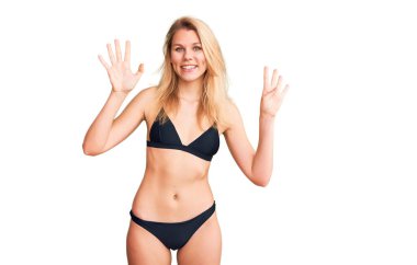 Genç, sarışın, bikini giyen güzel bir kadın dokuz numaralı parmaklarıyla gösteriş yapıyor ve gülümsüyor. Kendinden emin ve mutlu.. 