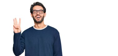 Gündelik kıyafetler giyen ve gözlük takan İspanyol genç adam üç numarayı gösterip işaret ederken kendinden emin ve mutlu bir şekilde gülümsüyor.. 