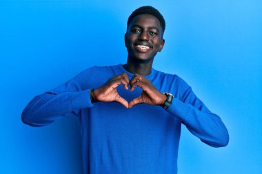 Genç Afro-Amerikalı sıradan kıyafetler giyen, aşık gülümseyen, elleriyle kalp sembolü yapan bir adam. romantik kavram. 