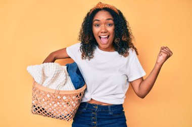 Genç Afrikalı Amerikalı kadın çamaşır sepetini tutarken gururla bağırıyor, zaferi kutluyor ve kollarını kaldırarak çok heyecanlanıyor. 