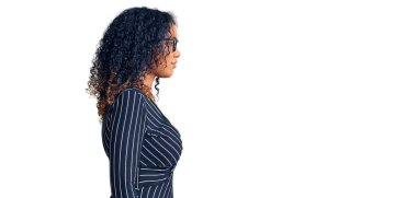 Afro-Amerikalı genç bir kadın günlük kıyafetler ve gözlük takıyor. Yan tarafa bakıyor, rahat poz veriyor, kendine güvenen bir gülümsemesi var.. 