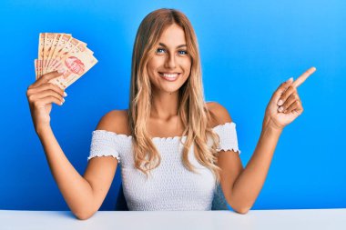 Güzel sarışın kadın elinde 100 Meksika pezosu tutuyor. Gülümsüyor, mutlu bir şekilde işaret ediyor. 