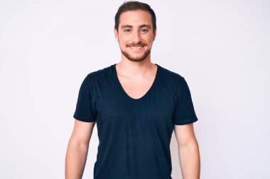 Gündelik kıyafetler giyen yakışıklı genç adam pozitif ve mutlu görünüyor. Duruyor ve gülümsüyor. Kendine güvenen bir gülümsemeyle dişlerini gösteriyor. 