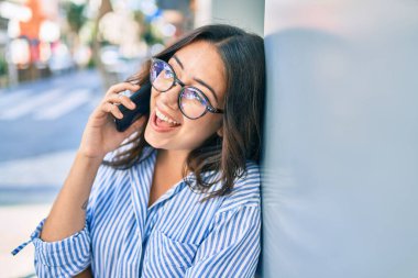 Genç İspanyol iş kadını gülümsüyor. Şehirdeki akıllı telefondan mutlu bir şekilde konuşuyor..