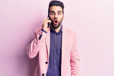 Sakallı genç yakışıklı adam akıllı telefondan konuşuyor. Korkmuş ve şaşırmış bir şekilde ağzı açık, inançsız bir yüz. 