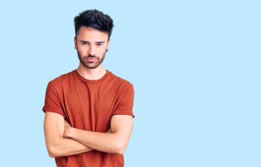 Gündelik kıyafetler giyen, kuşkucu ve gergin genç İspanyol bir adam. Yüzünde çapraz kollarla onaylamayan bir ifade var. negatif kişi. 