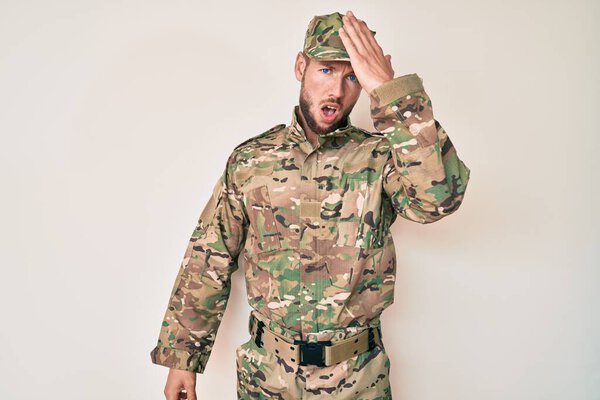 Young caucasian man wearing camouflage army uniform surprised with hand on head for mistake, remember error. forgot, bad memory concept. 