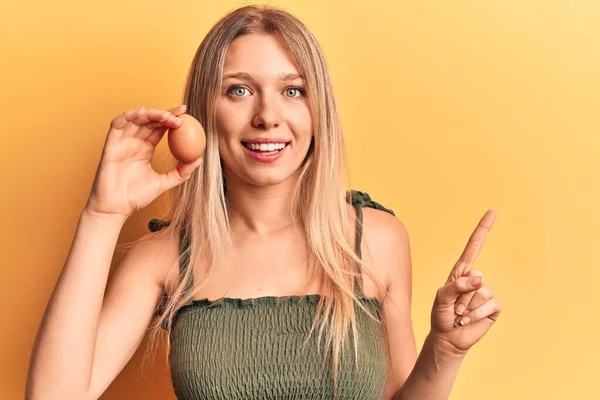 Young Blonde Woman Holding Egg Smiling Happy Pointing Hand Finger — ストック写真