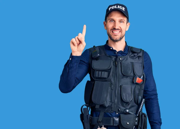 Young handsome man wearing police uniform showing and pointing up with finger number one while smiling confident and happy.