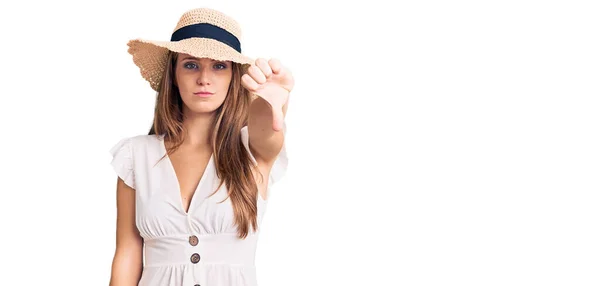 若い美しいブロンドの女性は夏のドレスを着て 帽子は親指を下にジェスチャーで拒絶と否定を示す不満と怒りを見ています 悪い表現 — ストック写真