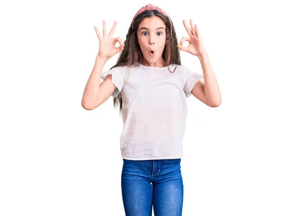カジュアルな白いTシャツを着たかわいいヒスパニック系の子供の女の子は驚いて 指でOk承認シンボルをやってショックを受けました クレイジーな表現 — ストック写真