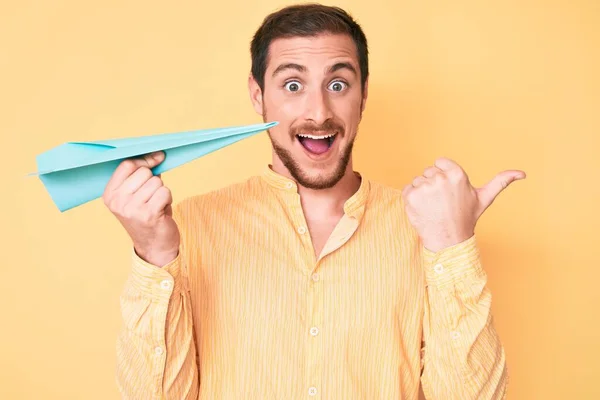 Joven Hombre Guapo Sosteniendo Avión Papel Apuntando Pulgar Hacia Lado — Foto de Stock