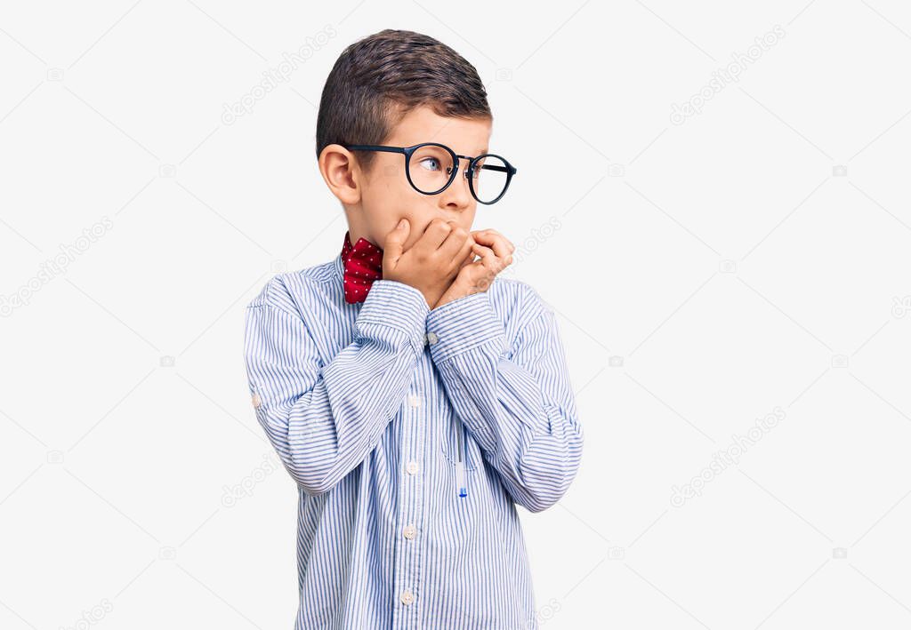 Cute blond kid wearing nerd bow tie and glasses looking stressed and nervous with hands on mouth biting nails. anxiety problem. 