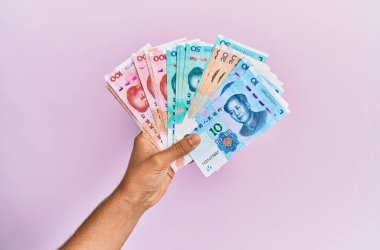 Hispanik el ele tutuşma Çin Yuan banknotları kapalı pembe arka plan.