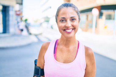 Şehirdeki orta yaşlı sporcu kadın gülümseyerek antrenman yapıyor.