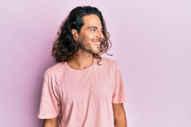 Uzun saçlı, sıradan kıyafetler giyen, rahat bir görünüm takınan, kendine güvenen, kendine güvenen genç, yakışıklı bir adam.. 