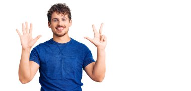Kıvırcık saçlı, rahat giyinen, 8 numaralı parmaklarıyla işaret eden, kendinden emin ve mutlu gülümseyen genç yakışıklı bir adam.. 