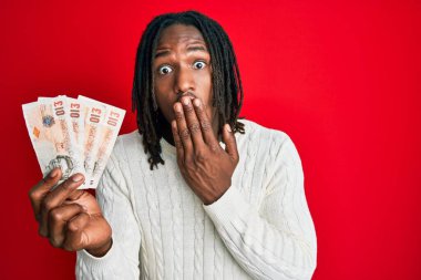 Saçları örgülü Afrika kökenli bir Amerikalı elinde 10 sterlin olan banknotlar ağızlarını eliyle kapatıyor, şok geçiriyor ve hata yapmaktan korkuyor. şaşırmış ifade 
