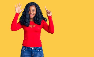 Güzel afro-amerikan kadın gündelik giysiler giyer ve 6 numaralı parmaklarıyla işaret ederken kendinden emin ve mutlu bir şekilde gülümserdi.. 