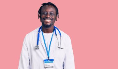 Doktor steteskop ve kimlik kartı takan genç Afro-Amerikan bir adam. Olumlu ve mutlu görünüyor. Kendine güvenen bir gülümsemeyle dişlerini gösteriyor. 