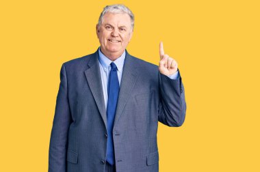 Kıdemli, gri saçlı, iş ceketi giyen bir numaralı parmağı gösteren ve mutlu bir şekilde gülümseyen adam.. 