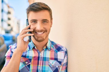 Genç beyaz adam gülümsüyor. Şehirdeki akıllı telefondan konuşuyor..