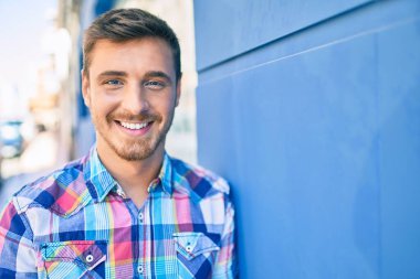 Beyaz bir adam gülümsüyor. Şehrin duvarına yaslanıyor..