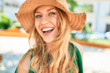 Yaz şapkası takmış, mutlu bir şekilde gülümseyen güzel sarışın bir kadın. Şehrin caddesinde yüzünde gülümsemeyle dikilirken.