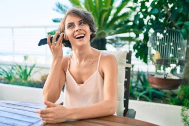 Genç, güzel, beyaz bir kadın evde mutlu bir şekilde gülümsüyor. Telefondaki bir sesli mesajı dinliyor.