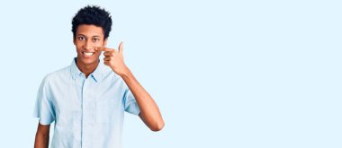 Genç Afro-Amerikan adam, günlük kıyafetler giyip, el ve burunla işaret ederek, neşeyle gülümsüyor. güzellik konsepti 