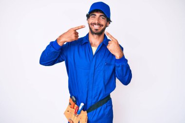 Kıvırcık saçlı, ayı gibi giyinen, neşeli gülümseyen ve parmakları, dişleri ve ağzıyla işaret eden yakışıklı genç adam. diş sağlığı kavramı. 