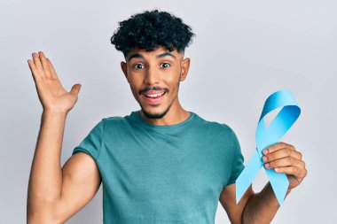 Genç Arap yakışıklı adam mavi kurdele tutuyor zaferi mutlu bir gülümsemeyle kutluyor ve kazanan el kaldırarak ifade ediyor 